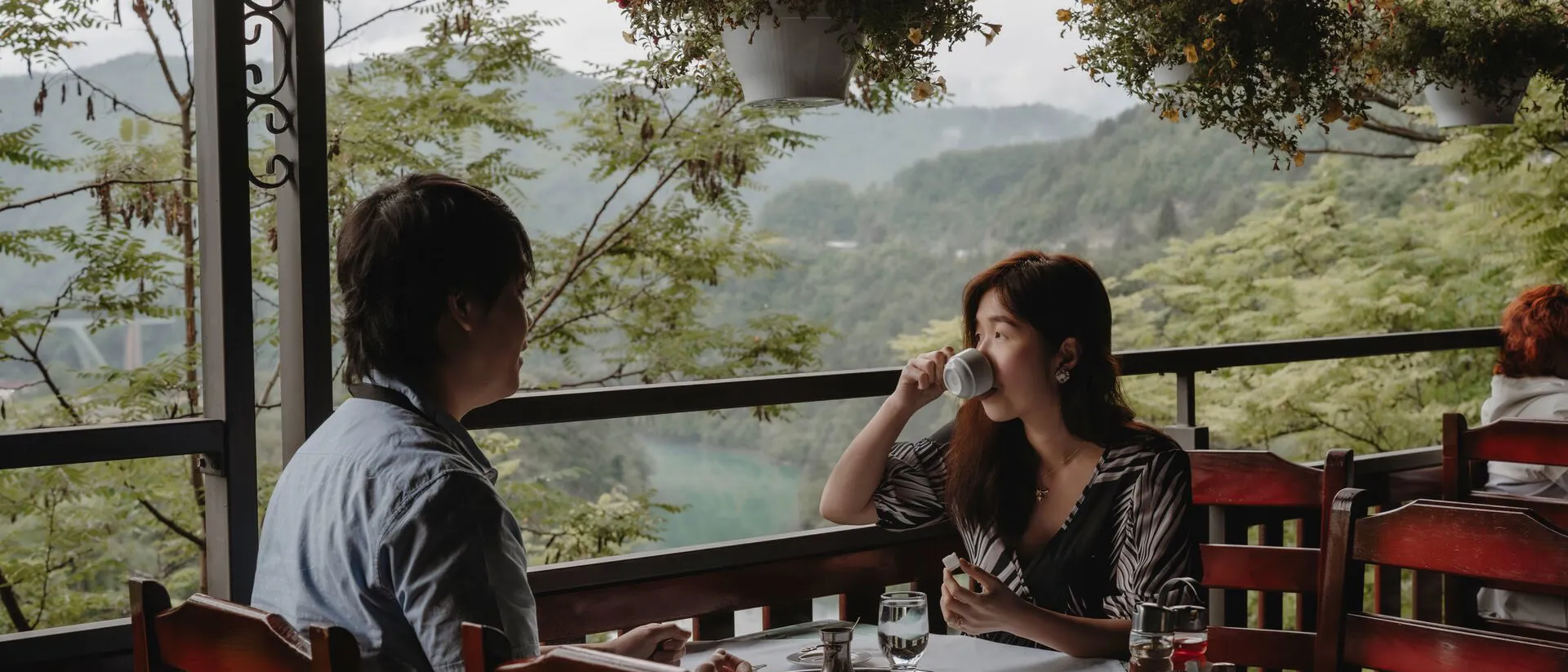 A couple eating breakfast on terrace with view on mountains covered with trees