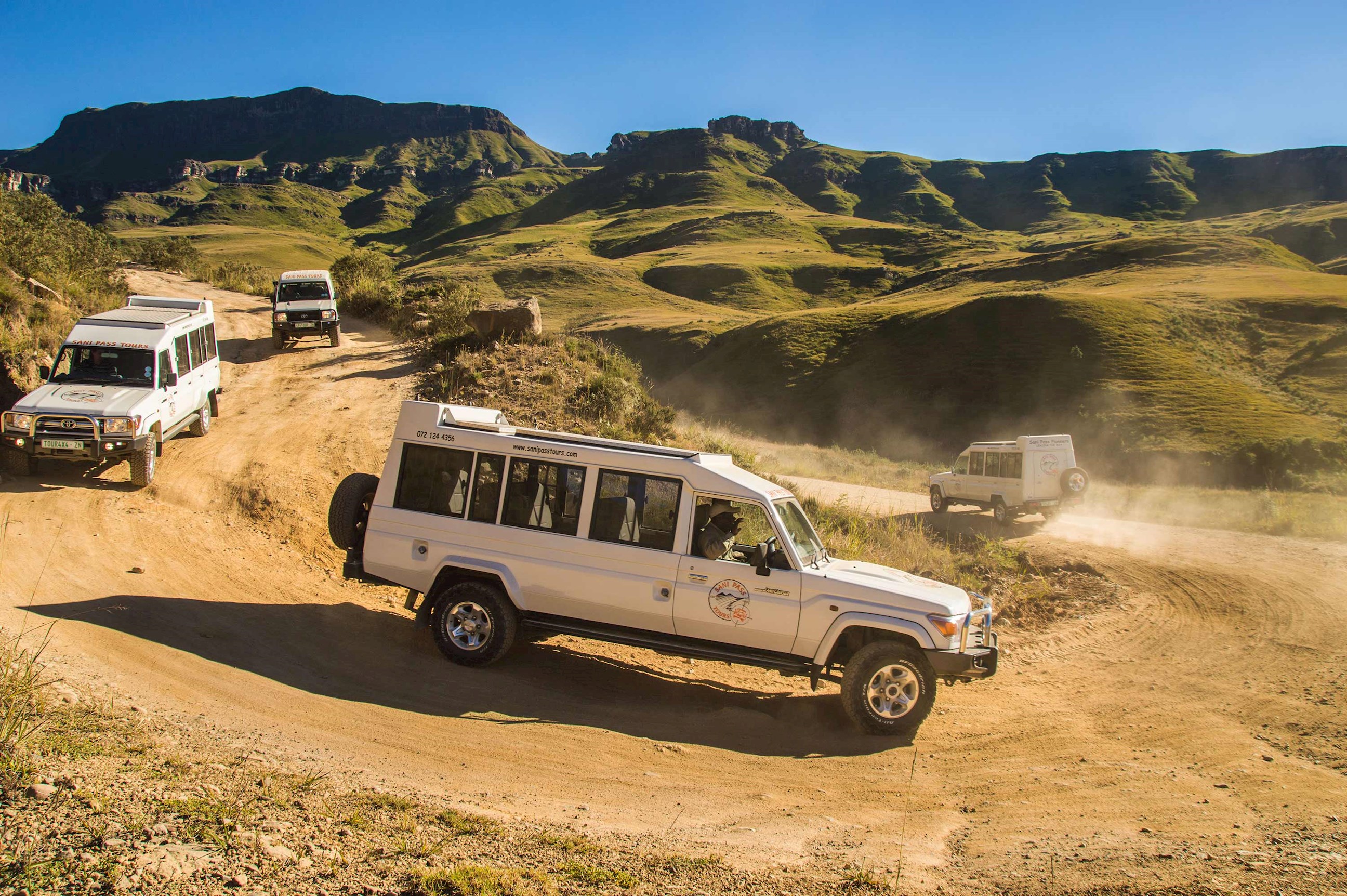 Four safari vehicles on dusty road, Sani Pass, South Africa