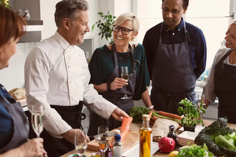Happy Chef Preparing Food While Teaching To Students Standing At Table