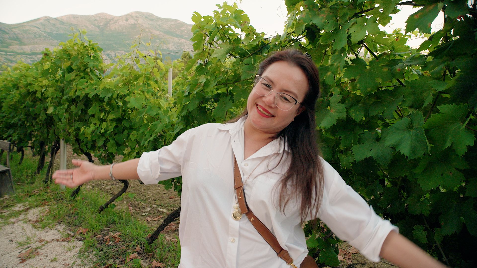 Smiling Woman In White Shirt Standing In The Middle Of Vines