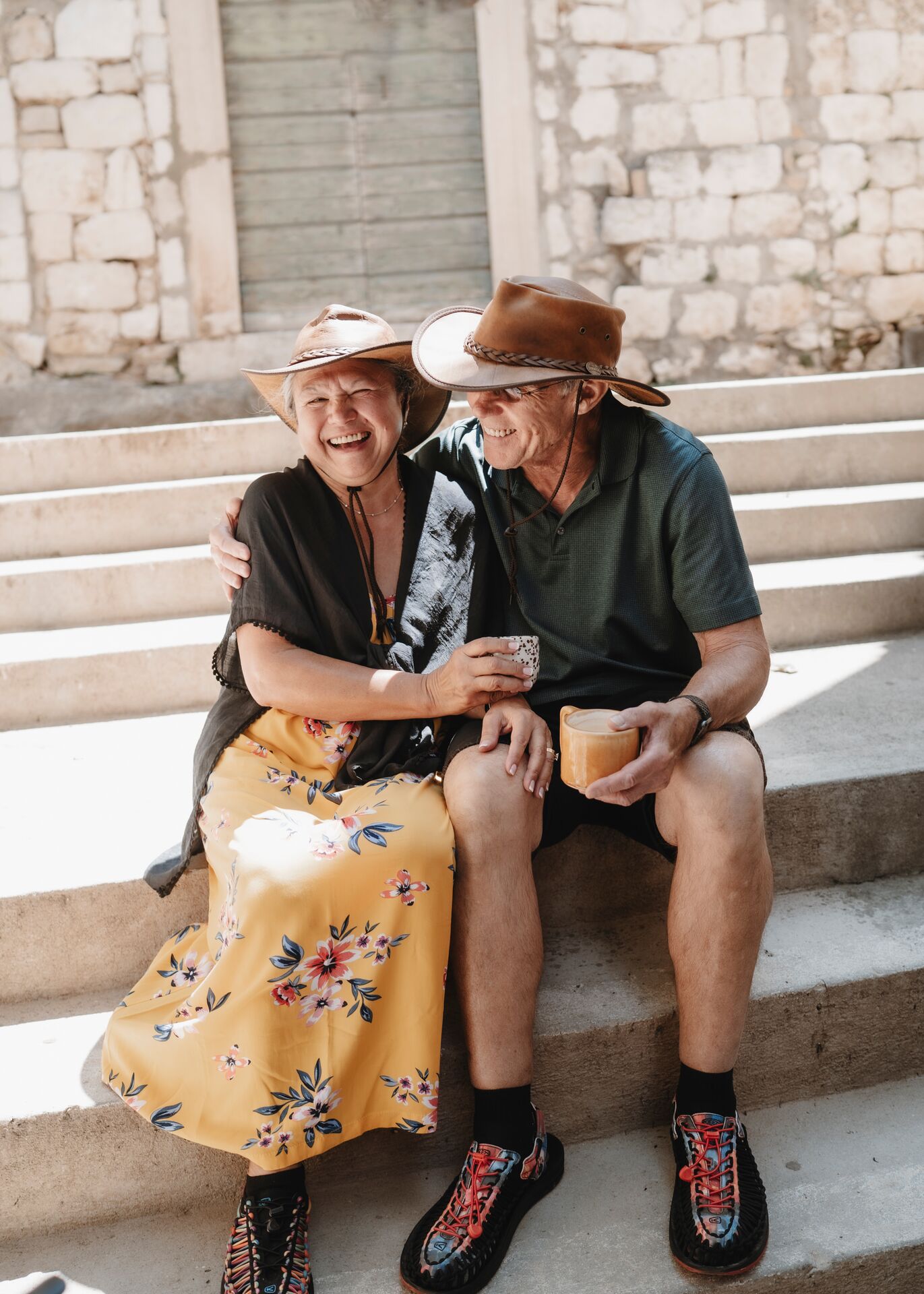 Elderly Couple In Hats Hugging And Sitting Outside On Stairs