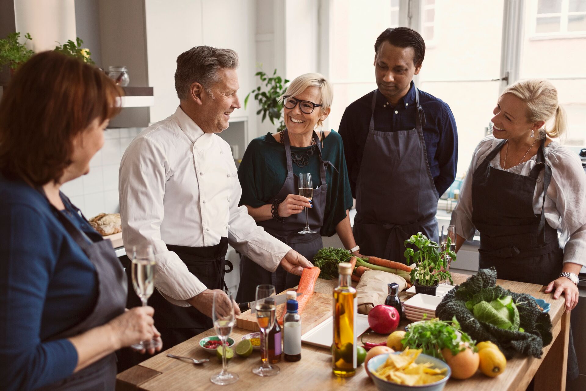 Chef smiling while surrounded by smiling guests and fresh ingredients