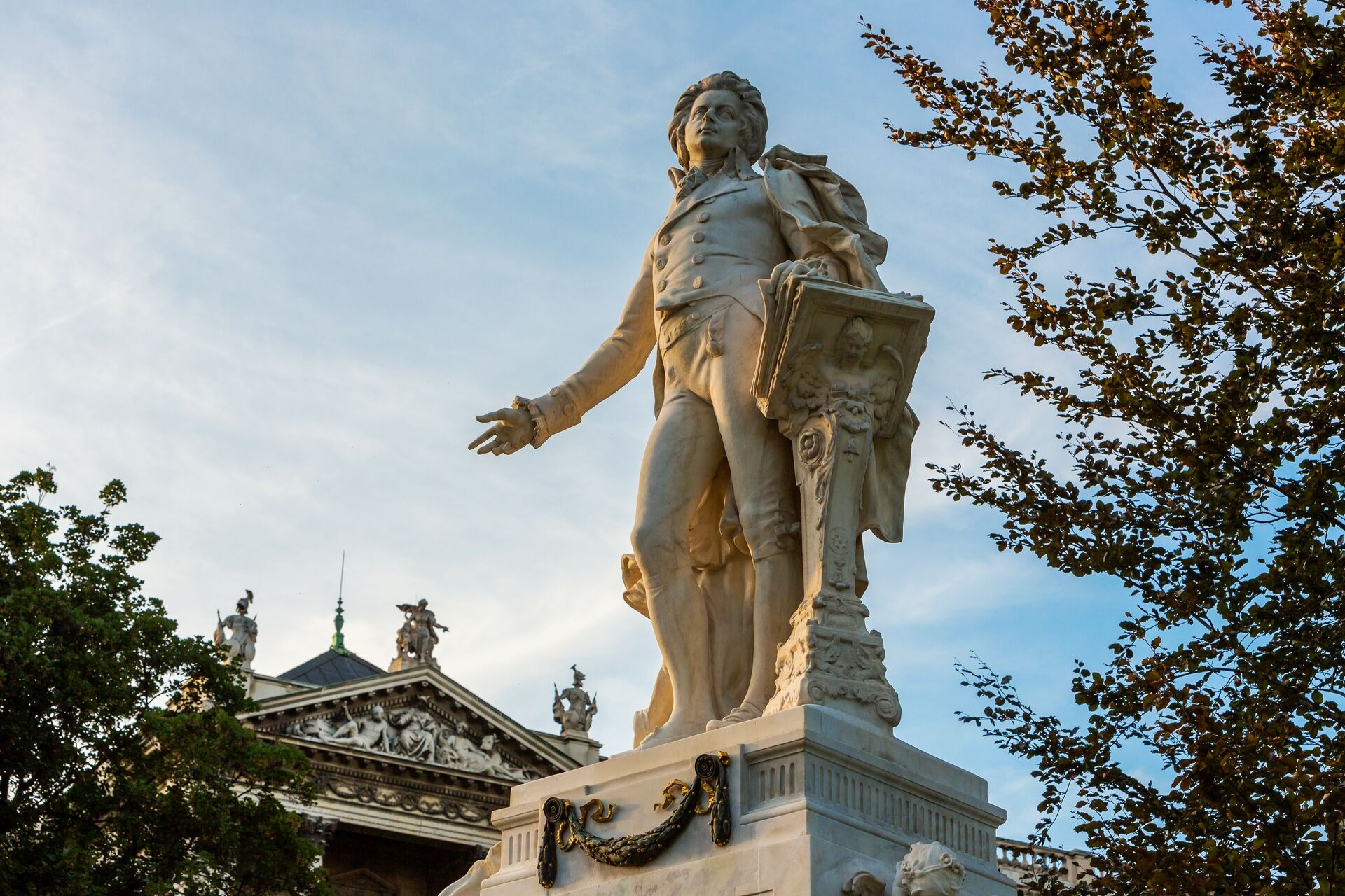 A marble statue of a classical composer standing on a pedestal outdoors.