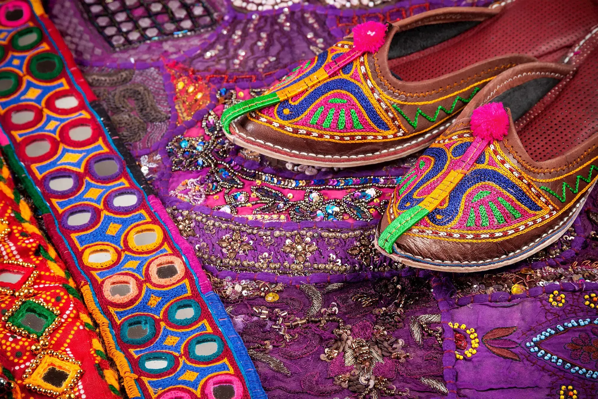 Colourful embroidered Indian shoes on vibrant decorative fabric background, Delhi, India