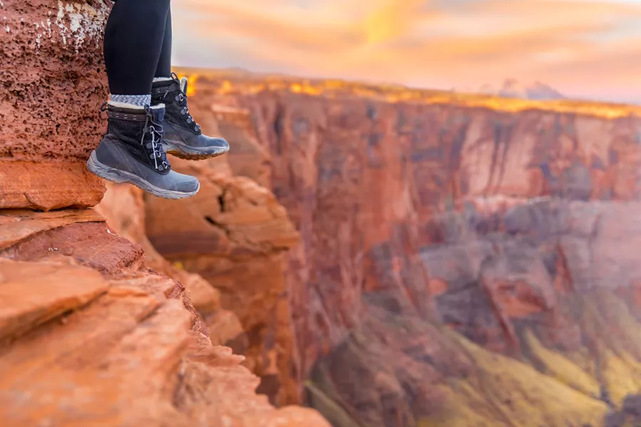Hiking boots dangling over a cliff at sunrise in Arizona, USA