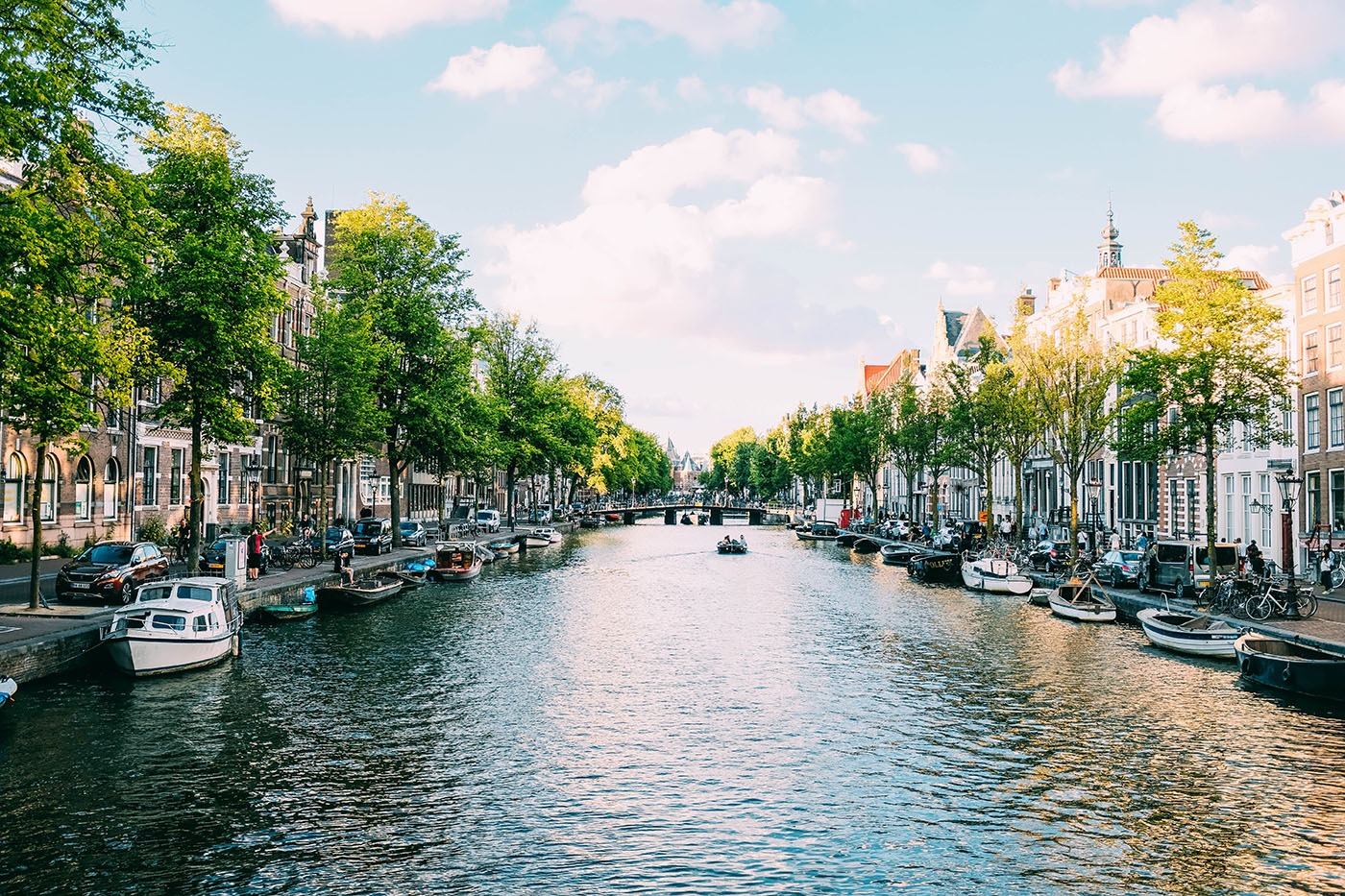 Photo Of A Wide Canal In Central Amsterdam Surrounded By Historic Townhouses Trees And Many Boats On A Sunny Day