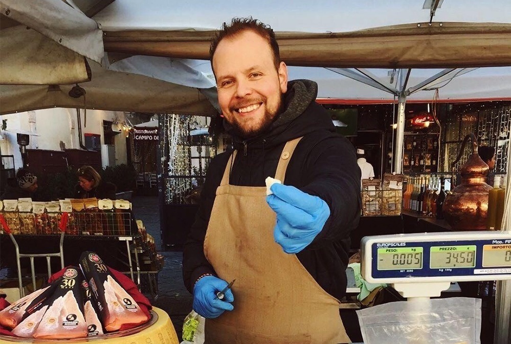 A seller in Campo de Fiori market giving away a piece of cheese to the clients