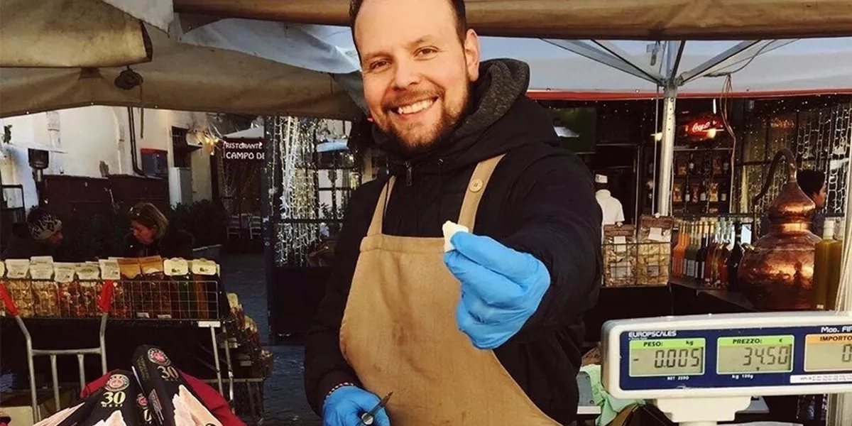 A seller in Campo de Fiori market giving away a piece of cheese to the clients