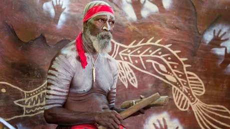 Aboriginal man sitting in front of traditional artwork in Australia