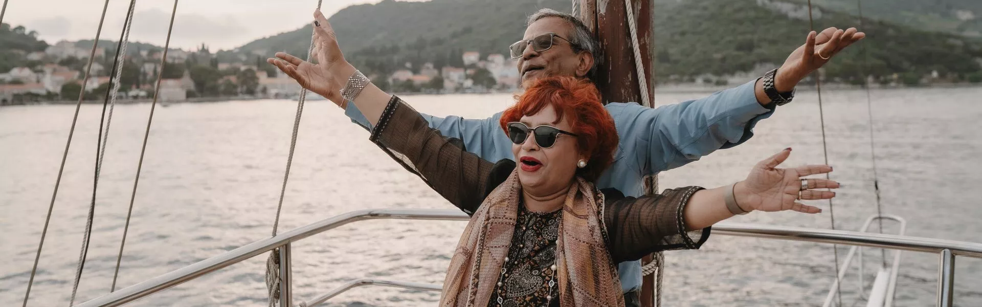 Two people stand at the stern of a boat holding their arms out
