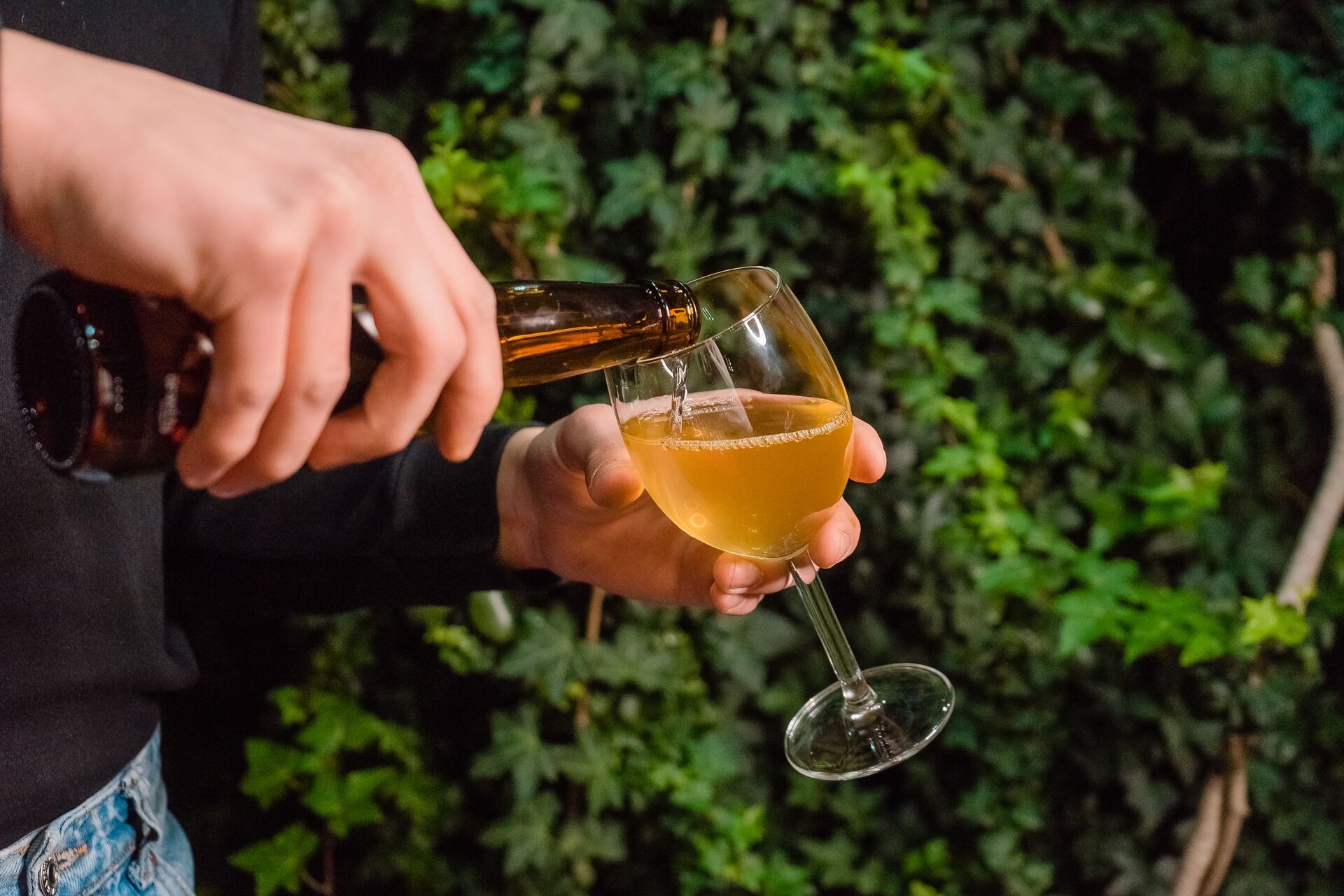 Large A Man S Hand Pours Cider Into A Glass A Waiter Holds A Sparkling Drink Against A Background Of Greenery