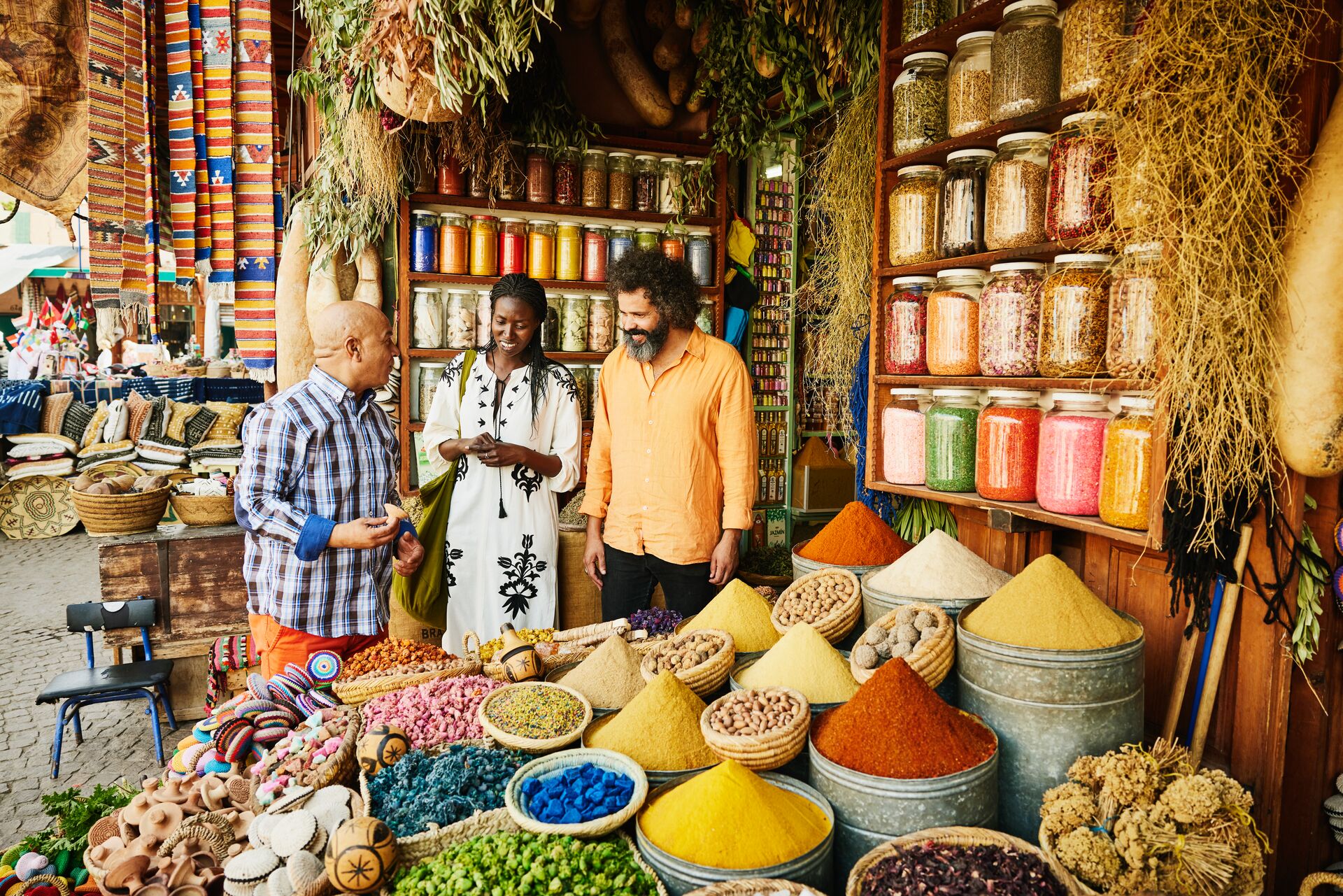 Wide Shot Couple Talking To Spice Shop Owner In The Souks Of Marrakech, North Africa