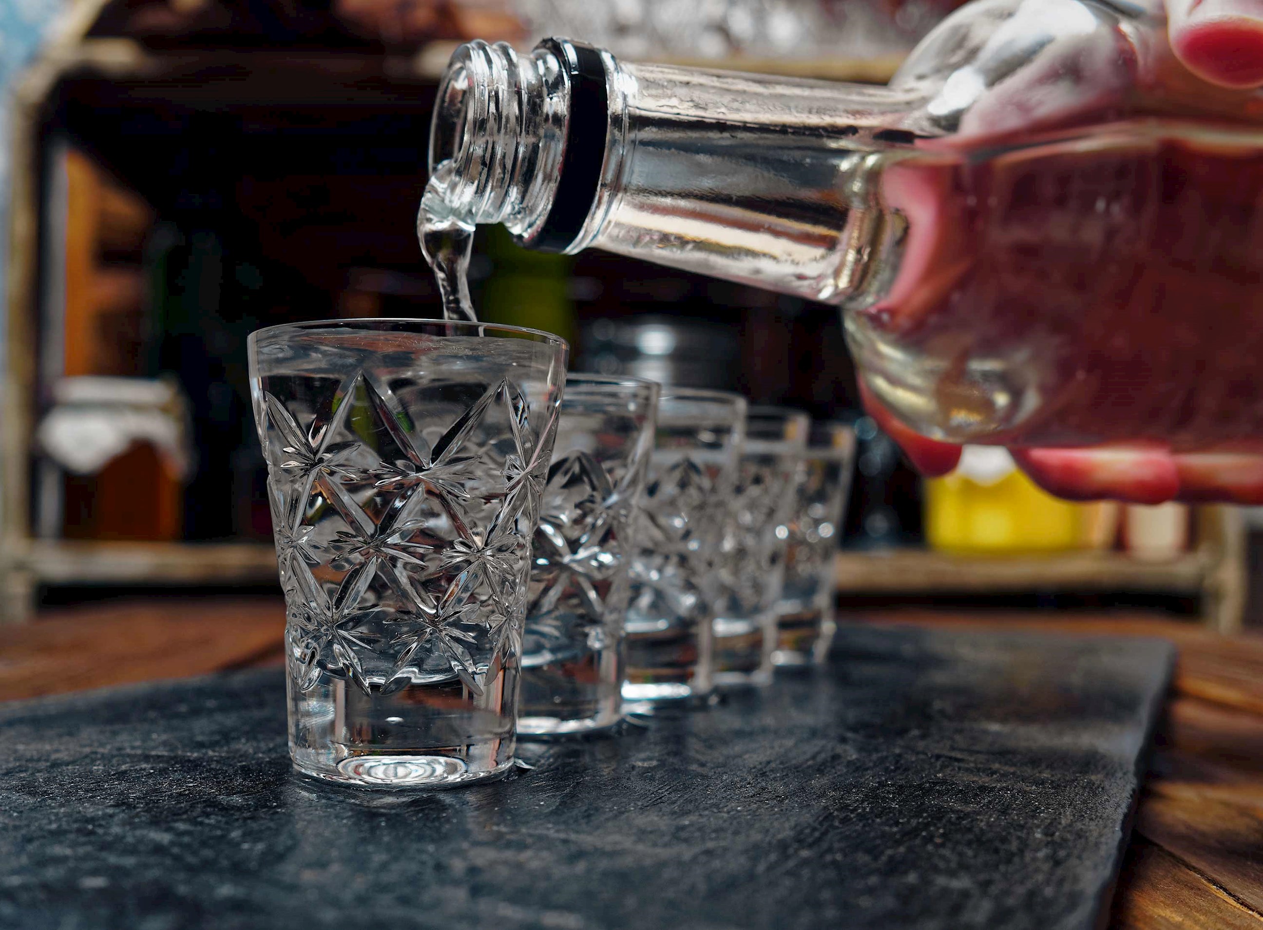 Vodka being poured from a glass bottle into crystal shot glasses