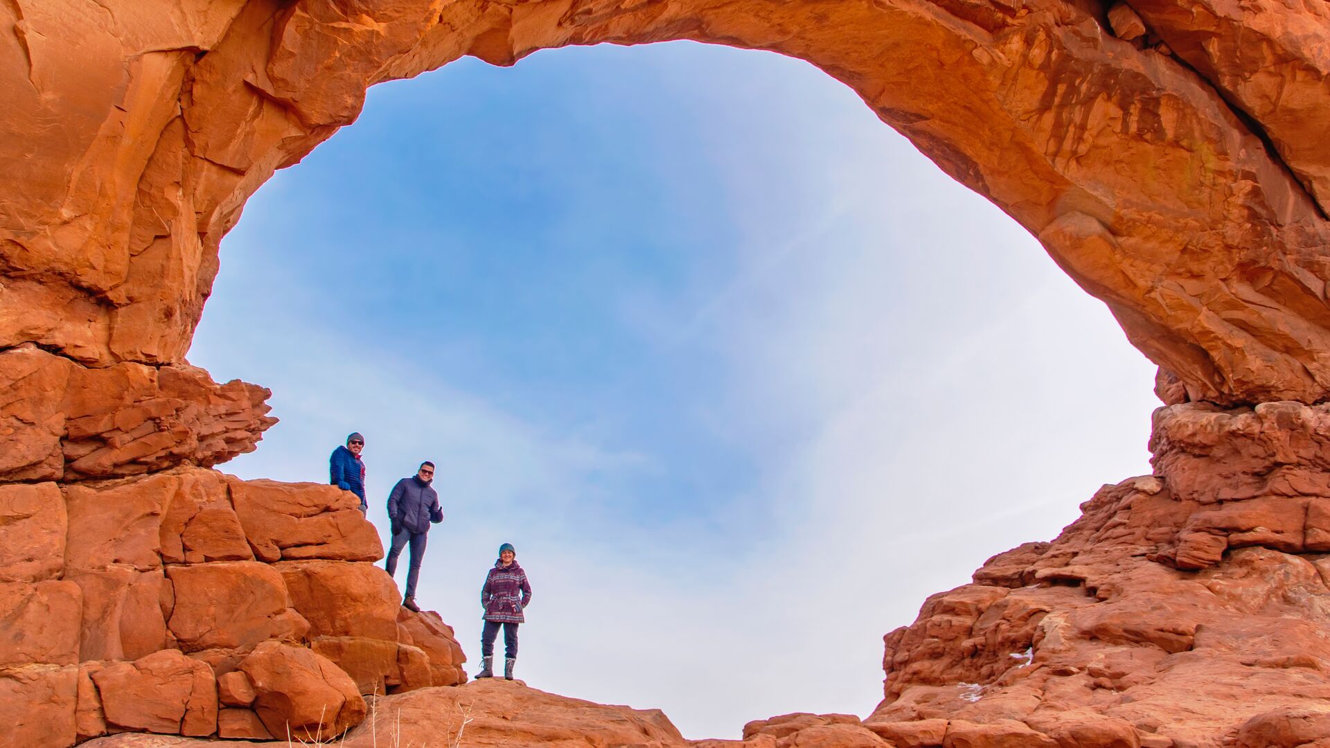 Three hikers standing under The North Window Arch in Arches National Park in Utah, USA