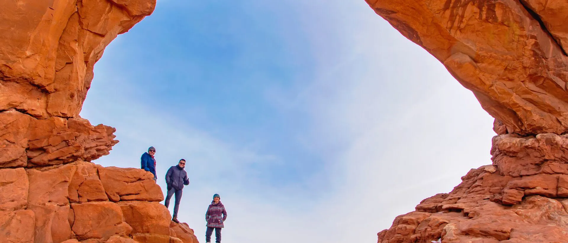 Three hikers standing under The North Window Arch in Arches National Park in Utah, USA