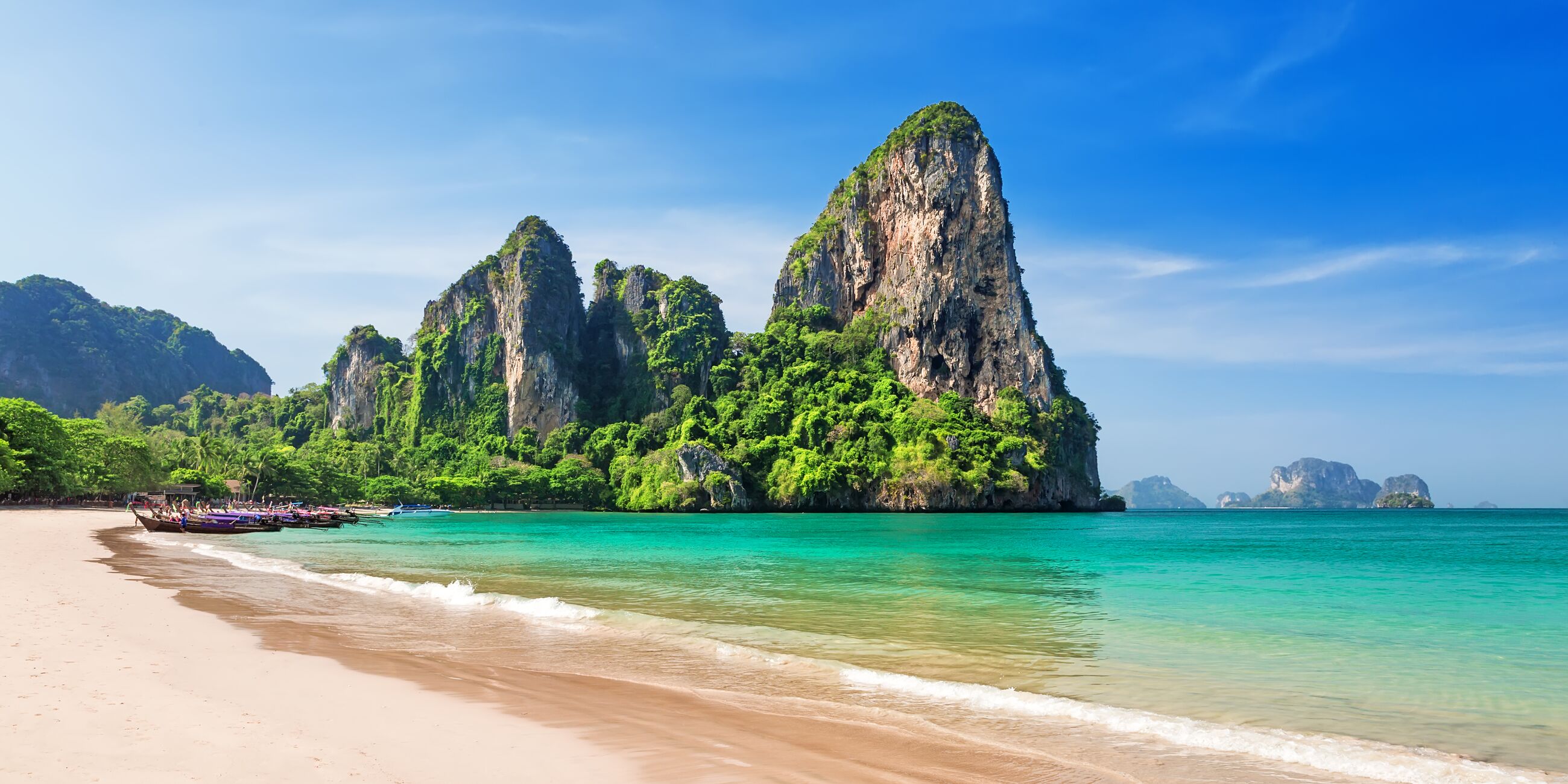 Traditional boats on Railay beach with rocky cliffs in Thailand 
