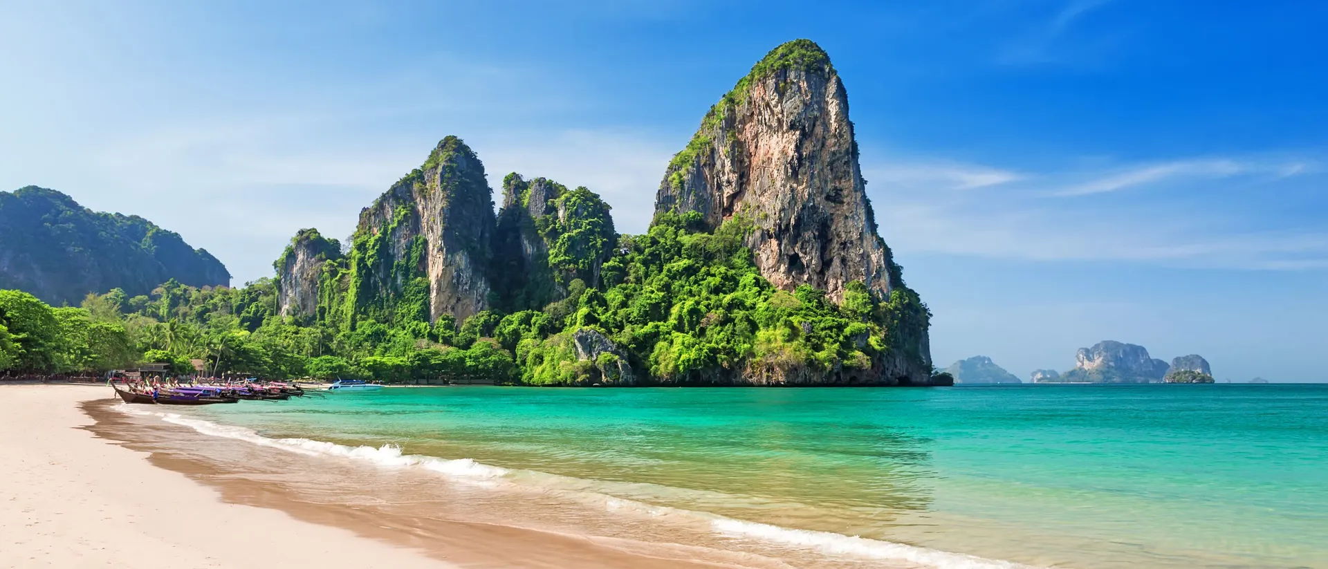 Traditional boats on Railay beach with rocky cliffs in Thailand