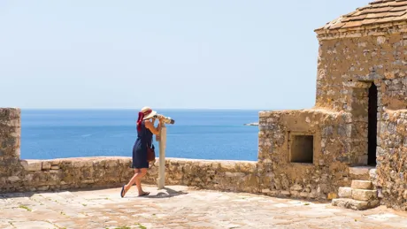 Woman in blue dress and straw hat watching the sights through binoculars