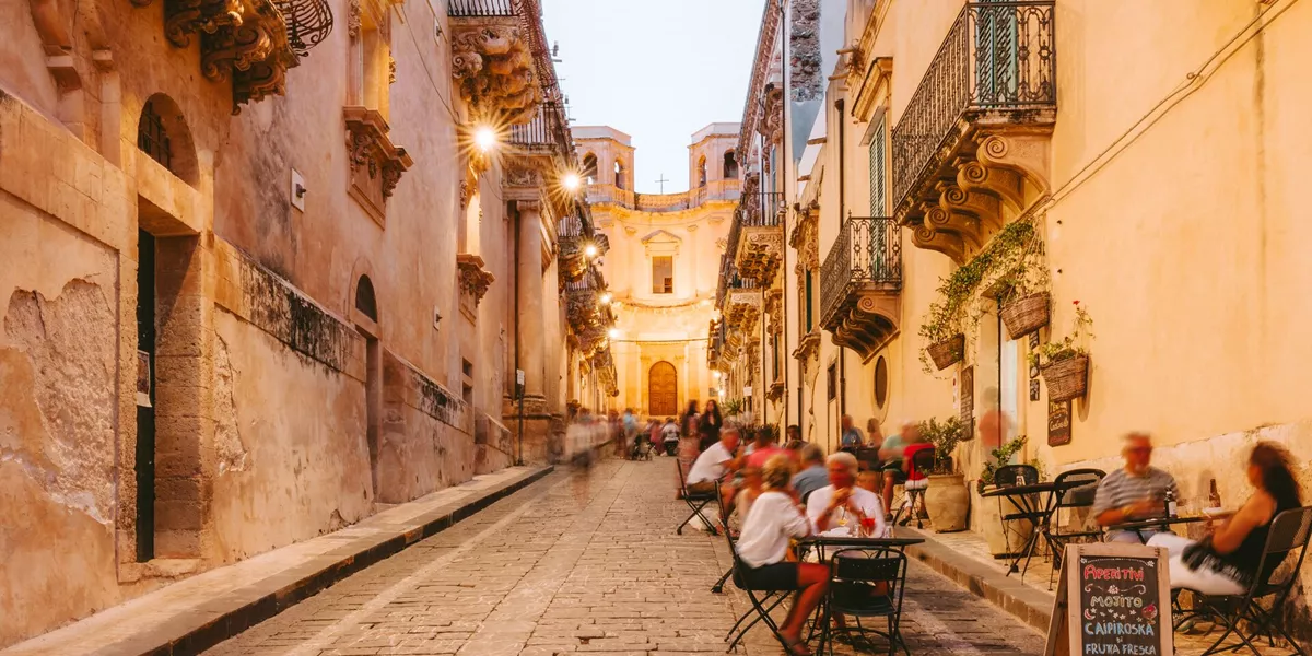 People dining outside restaurants and bars at dusk in Noto, Italy