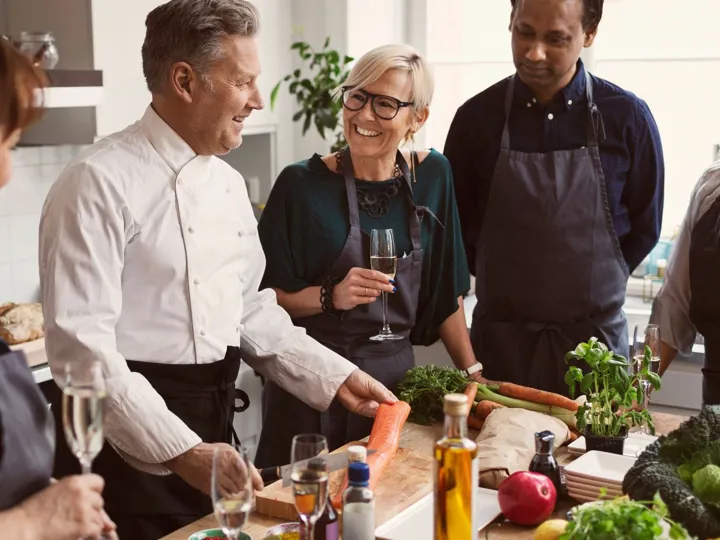 Happy chef preparing food while teaching to students standing at table Happy Chef Preparing Food While Teaching To Students Standing At Table