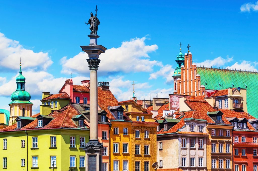 Travel on a Budget in Europe. Close up of colorful buildings in Warsaw, Poland. Orange, yellow, green, and red buildings, with bright blue sky with some clouds.