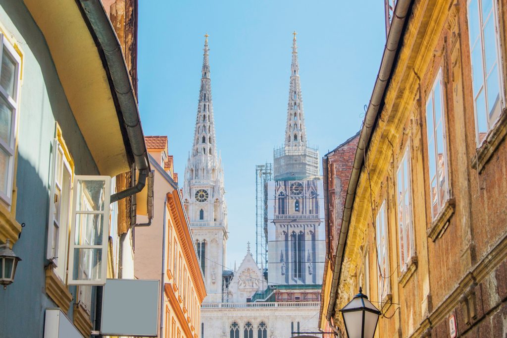Budget-friendly destinations in Europe. Top of Zagreb Cathedral in the center of the image, with the tops of buildings on either side.