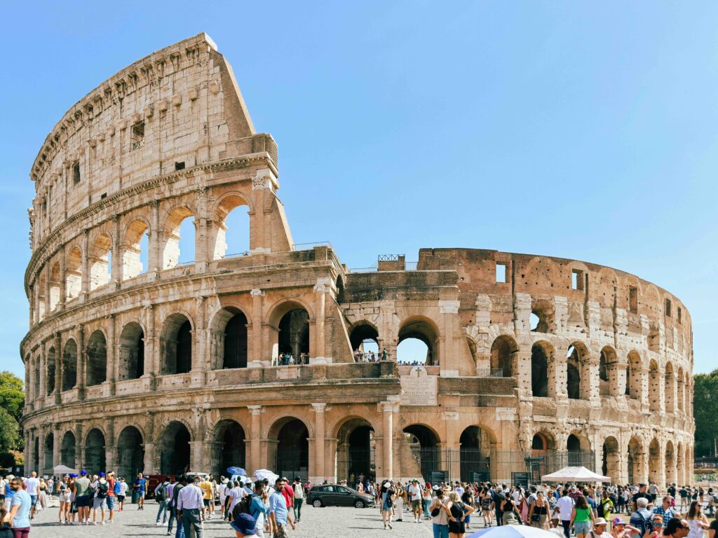 The ancient Roman Colosseum in Italy - a European landmark - under a bright blue sky, showing its weathered stone arches and partially intact outer wall.