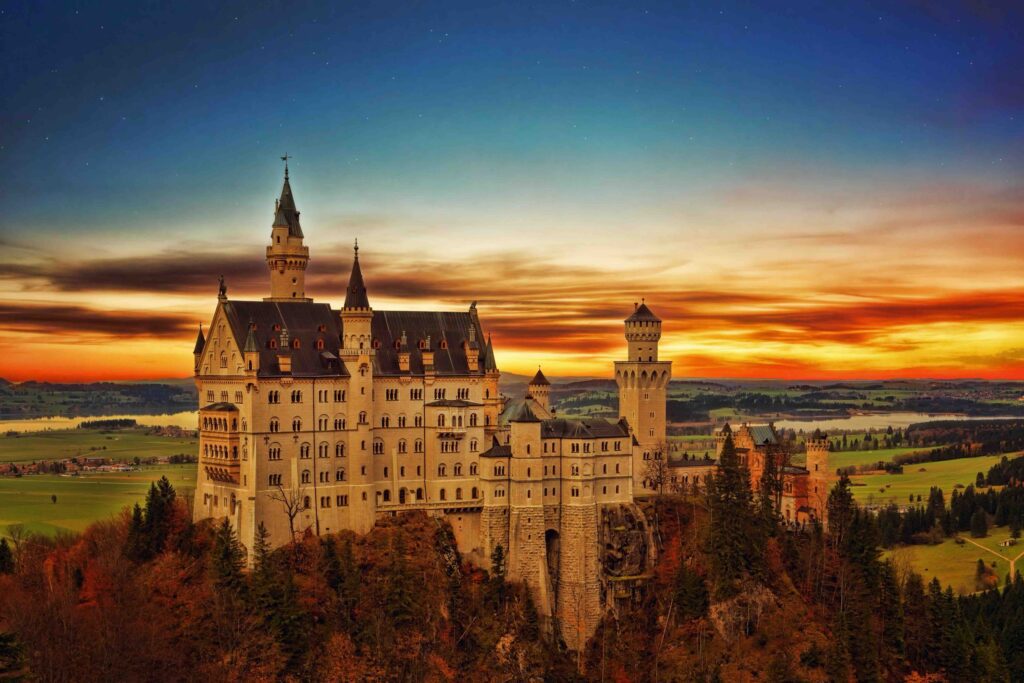 Neuschwanstein Castle in Germany, bathed in the warm glow of sunset, with its white towers rising above forested hills.