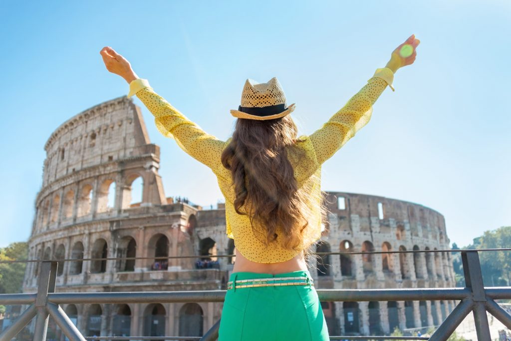 A woman standing with arms outstretched in front of the colosseum in Rome