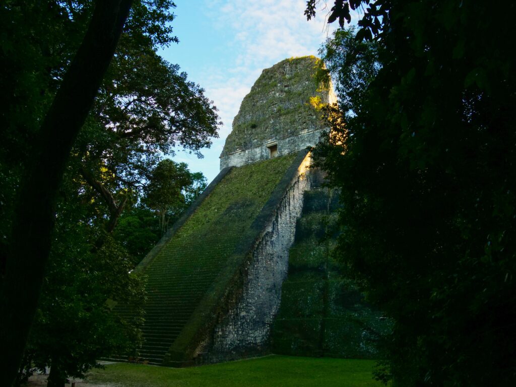 A dark photo of the structure in Tikal looming over, with dark trees on either side in the foreground
