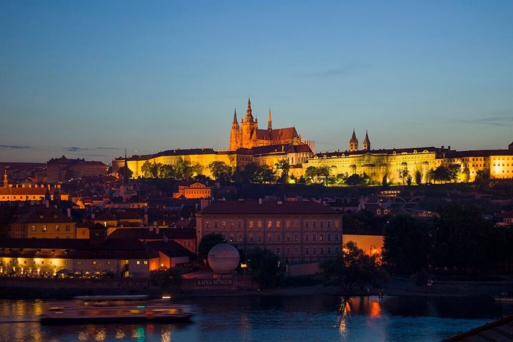 Dusk, sunset glow on the buildings. River in the forefront, buildings in the background with the Prague Castle visible in the background.