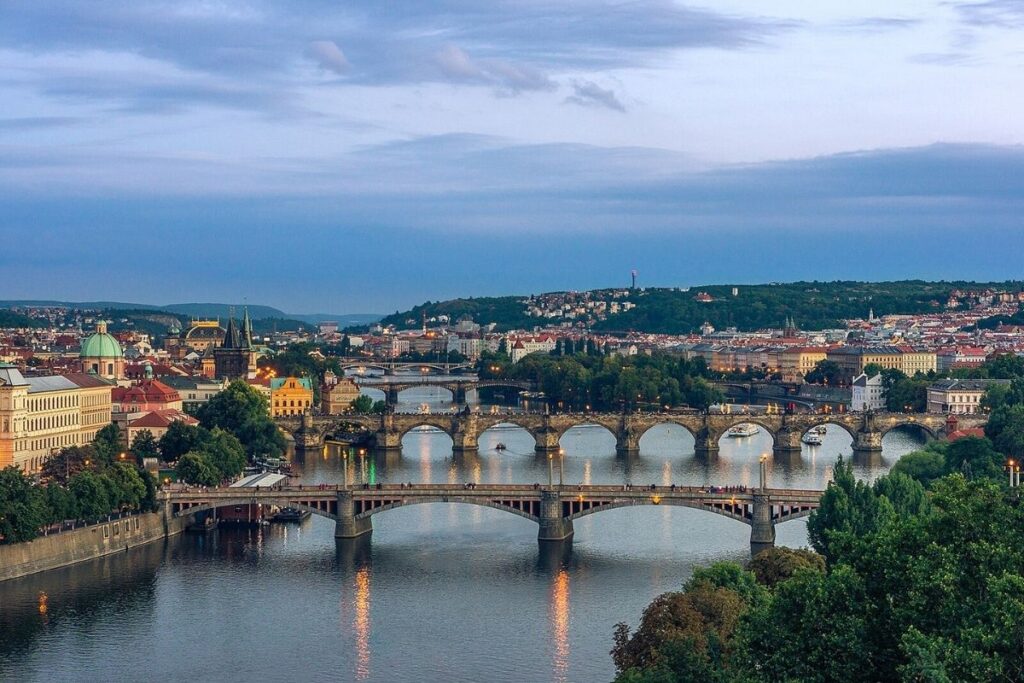 Three bridges in Prague, greenery and trees on the outside of the bridges and buildings further out.