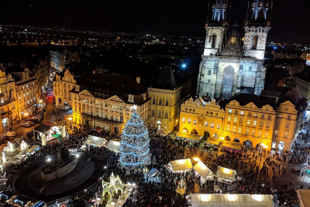 Birds-eye view of Christmas markets in Prague, giant Christmas tree in the middle and stalls surrounding it. Night time.