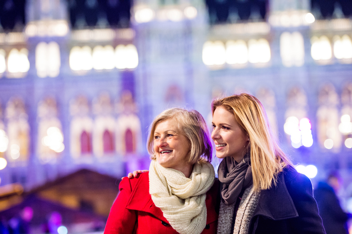 Two beautiful women, mother and daughter in winter clothes on a walk in illuminated night city. Historical building. Vienna, Austria. Travel with your mum