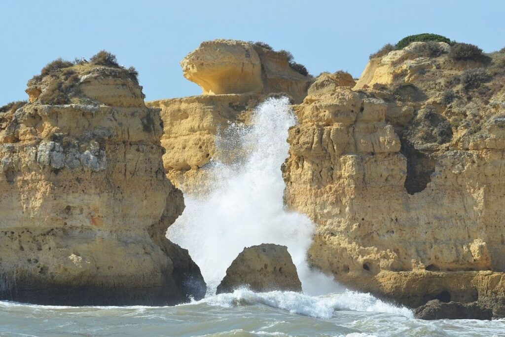 Cliffs in Portugal, with water splashing up against the side of them. Clear skies.