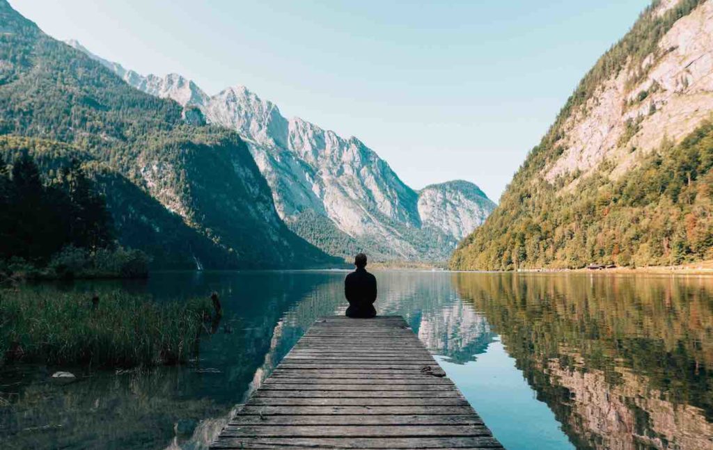 man sitting on pier by lake