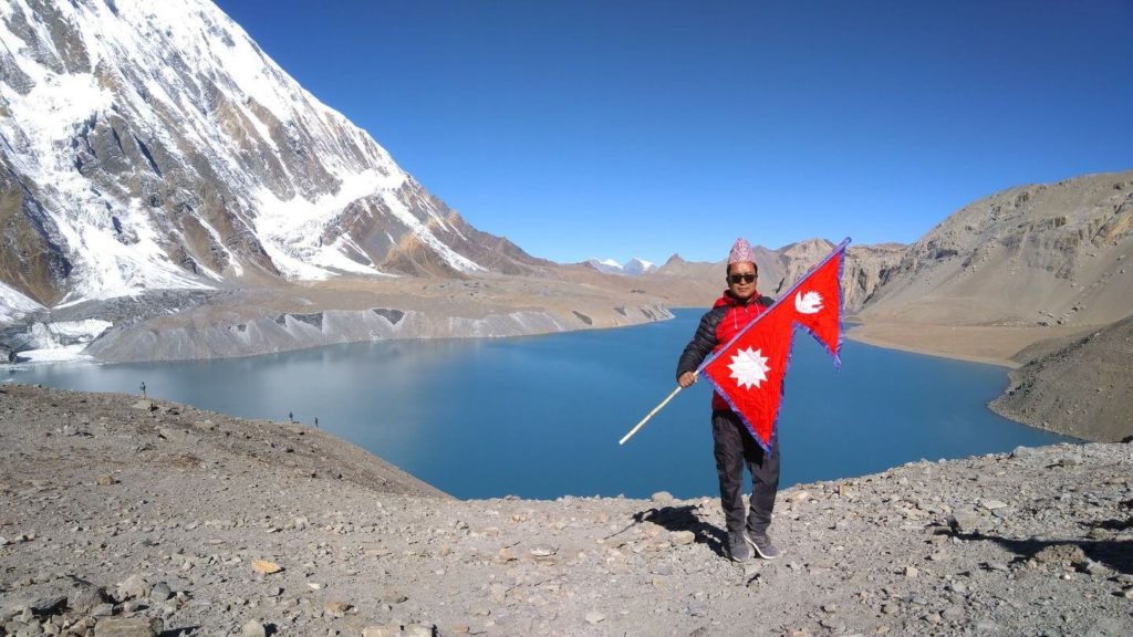man holding Nepal flag blue lake Himalayas