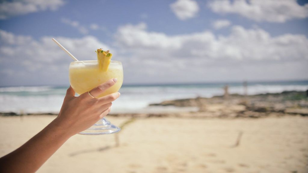 hand holding pina colada on beach
