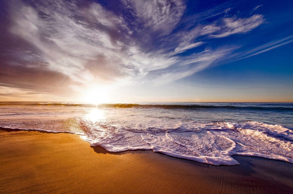 The sun is setting over a beach with waves in California.