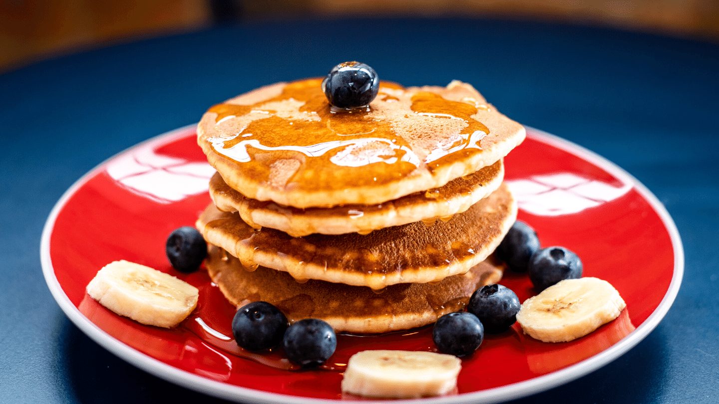 Maple syrup poured over Pancakes with blueberries and banana