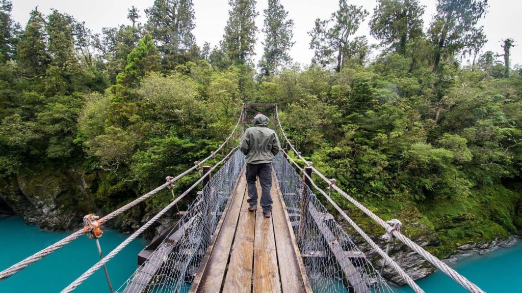 person walking along suspension bridge over blue river