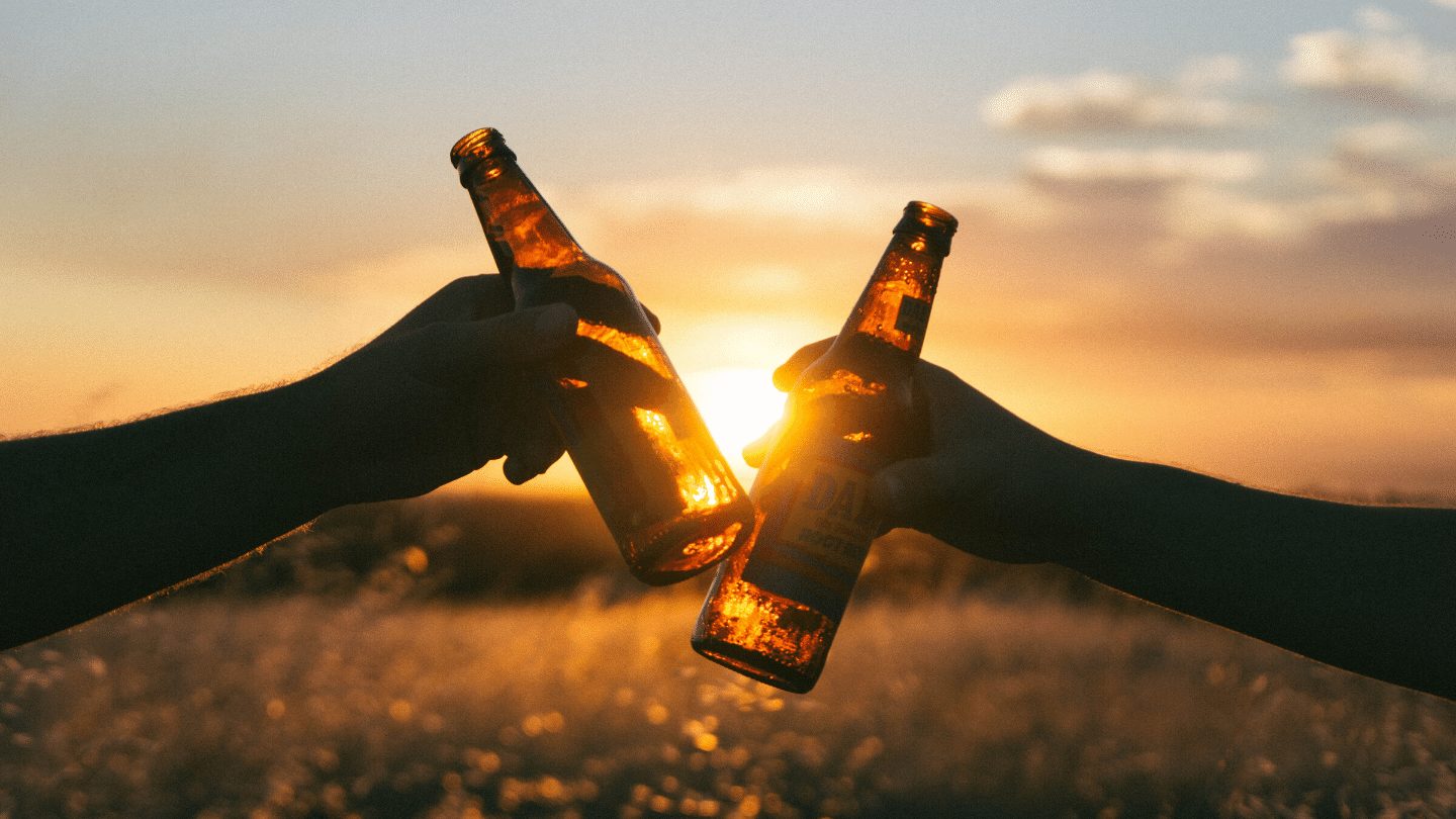 Hands holding two beer bottles at sunset