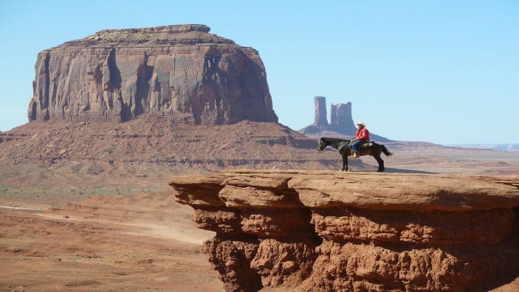 man riding horse among sandstone towers of Monument Valley USA