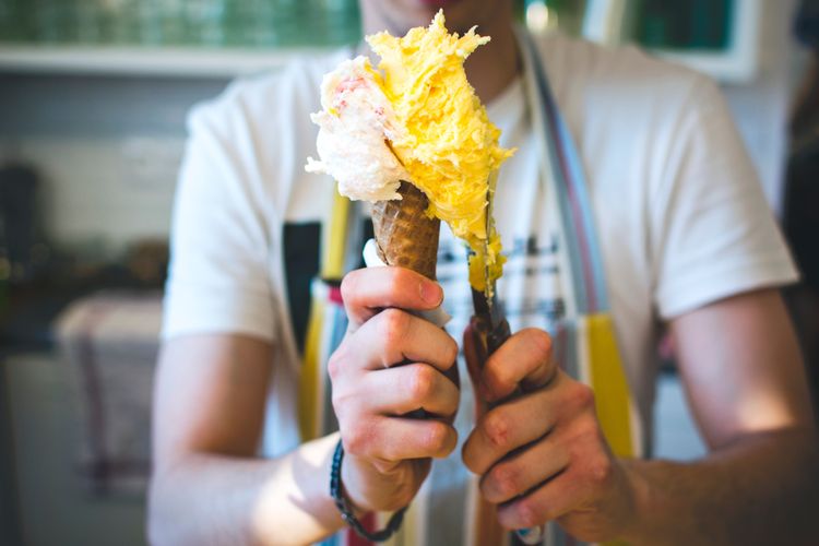 A server placing a scoop of yellow gelato against a white scoop atop a cone.