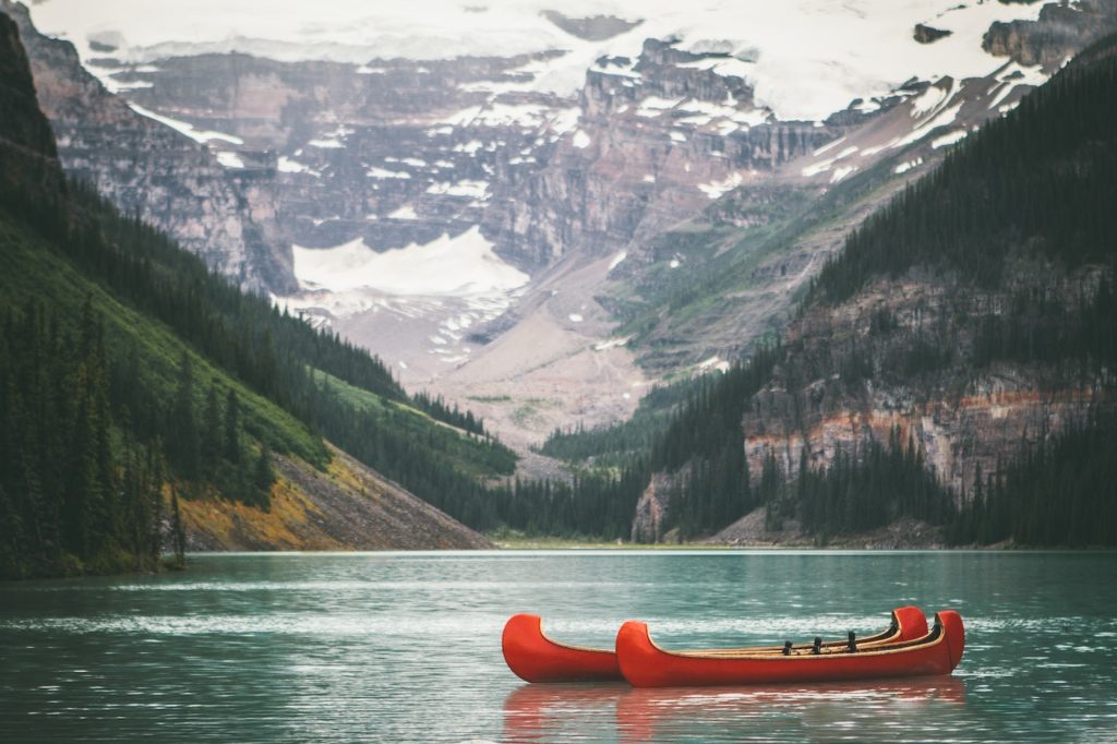 An orange canoe floating on a calm mountain lake with snowy peaks in the background, reminiscent of the tranquil and picturesque landscapes found in both the USA and Canada.