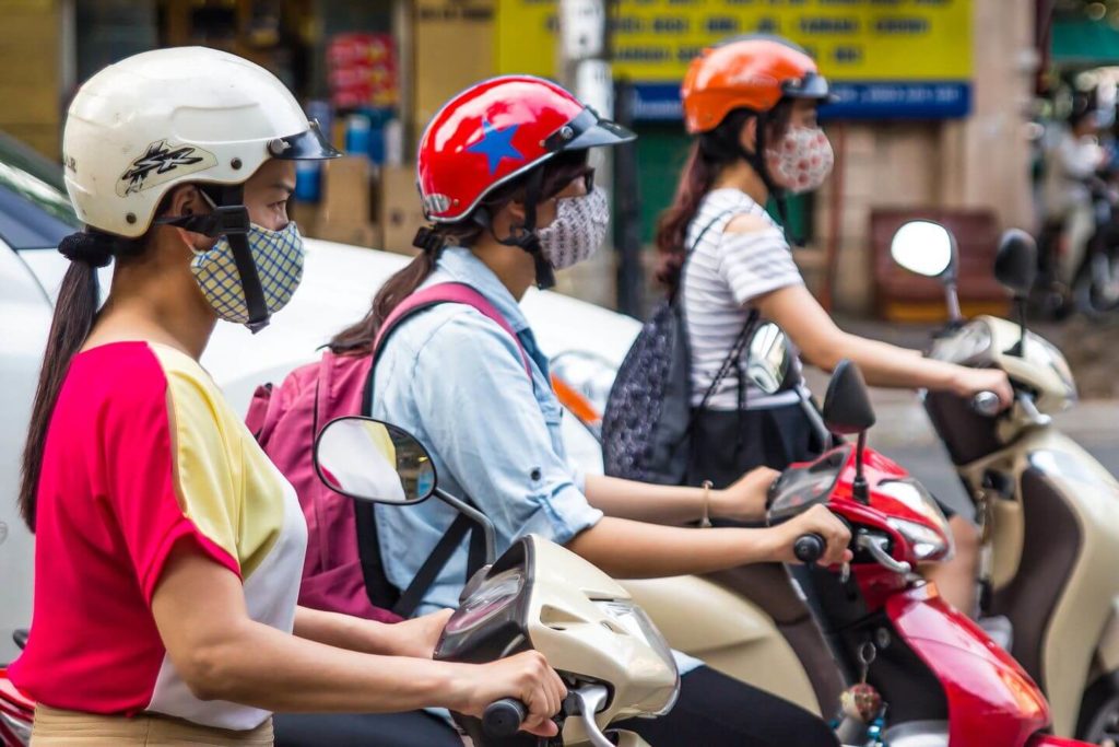 women on scooters wearing masks crossing the road in Vietnam