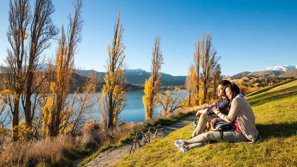 Young couple sitting on a hill looking at a river in New Zealand.