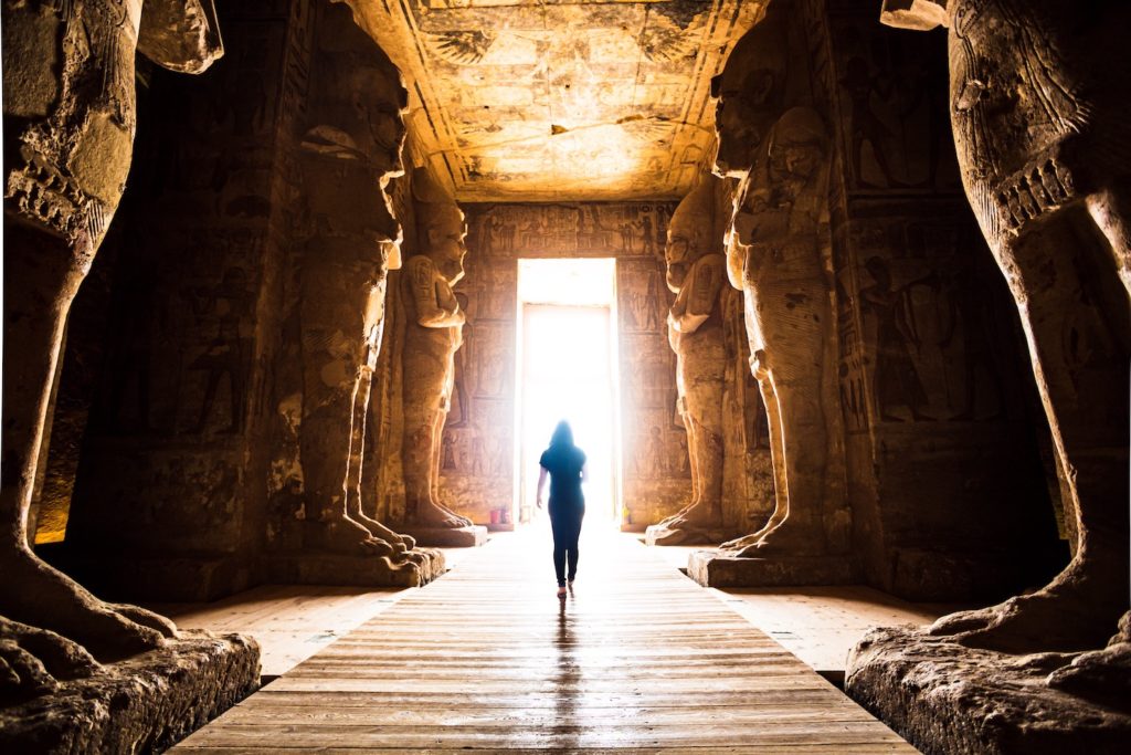 Woman walking through Egyptian temple towards open door 