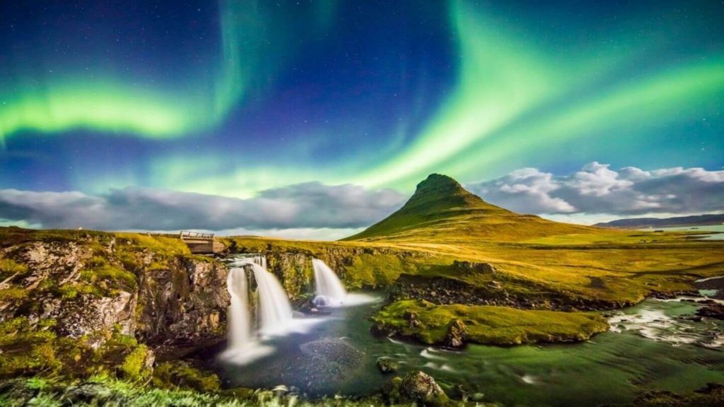 green northern lights over waterfalls and lush mountains Iceland