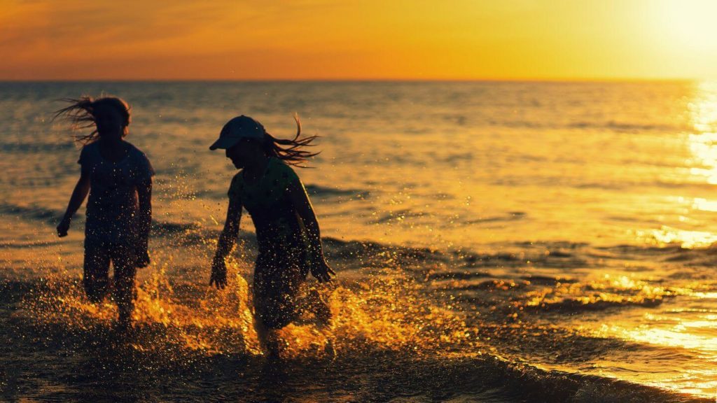 two girls splashing in the ocean at sunset